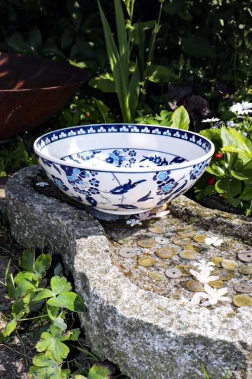 Handmade unique ceramic bowl with blue floral motifs on a white backdrop, seen from the side